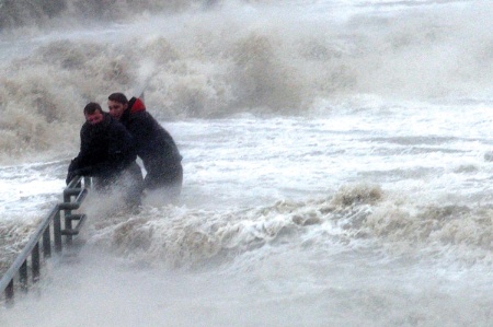 Men clinging to railings among strong waves