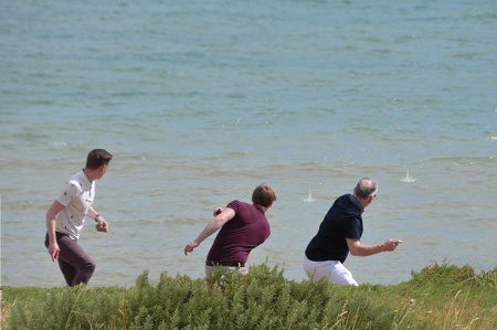 Three men skipping stones on sea