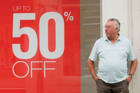 Man standing next to '50% off' sign in shop window