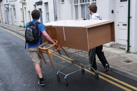 Male students moving furniture on shopping trolley
