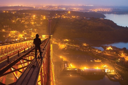 Young man walking along suspension bridge at night