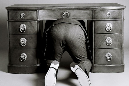 Man in suit hiding beneath desk