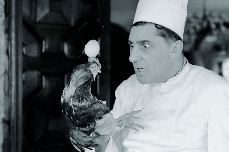 Male chef holding chicken by legs
