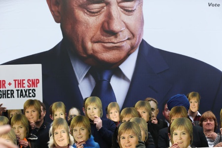 People wearing Nicola Sturgeon face masks in front of a large poster of Alex Salmond