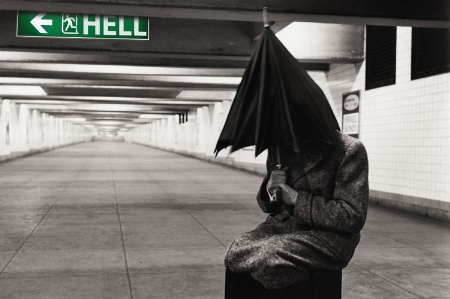 Man hiding beneath umbrella next to 'Hell' sign